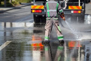 Worker and cistern truck washes and disinfects the asphalt. Cleaning and disinfects the streets with water truck.
